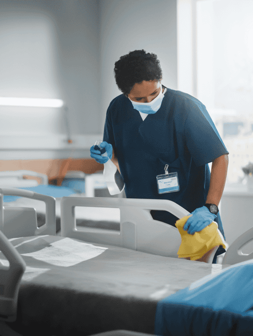 female healthcare worker wearing navy scrubs cleaning hospital bed