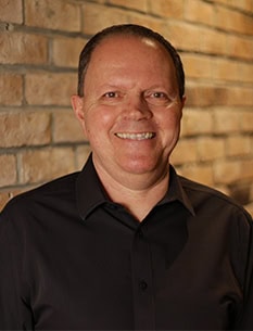 Male standing on a brick wall smiling