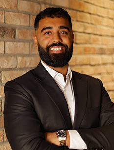 Man in suit standing on a brick wall arms crossed smiling